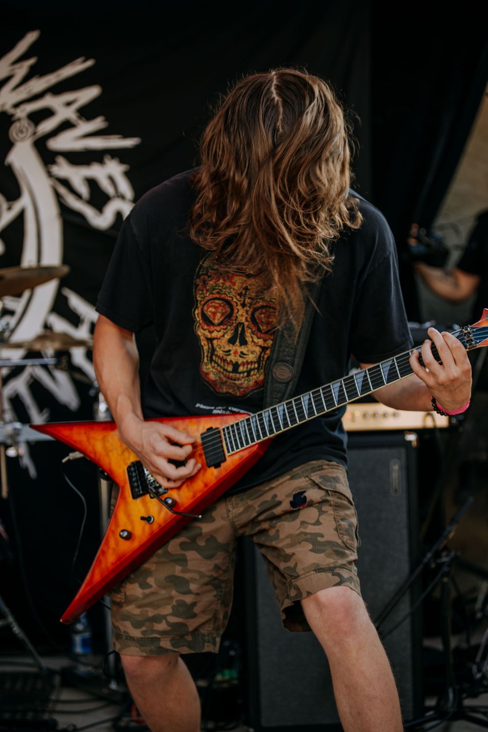 Guitar player performing with orange flying V guitar against black backdrop.