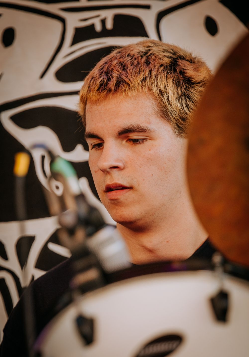 Close up of a performer with blonde hair in front of a dark background with white tribal graphics.