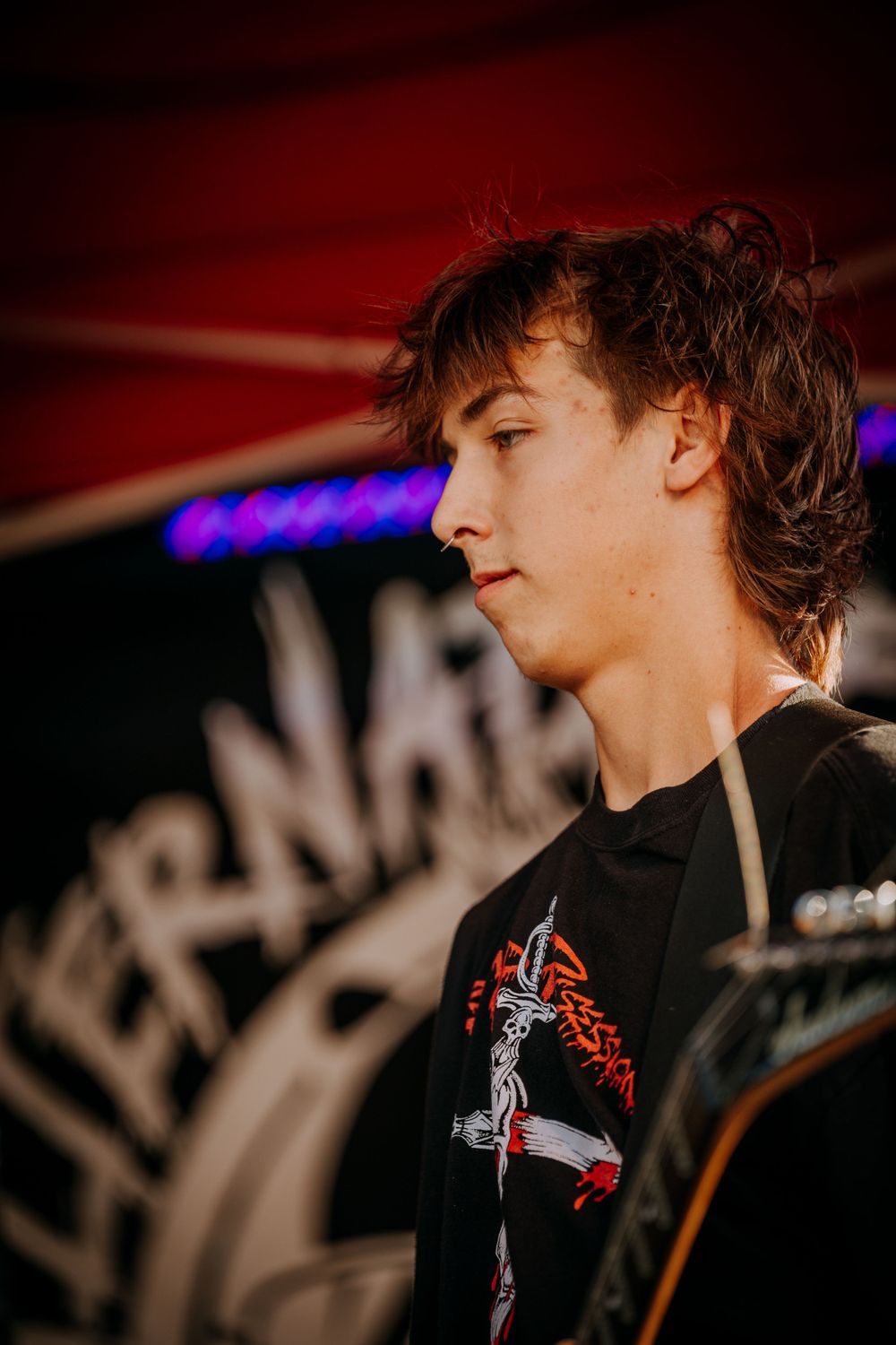 Side profile of a musician in a black t-shirt performing against a red backdrop.