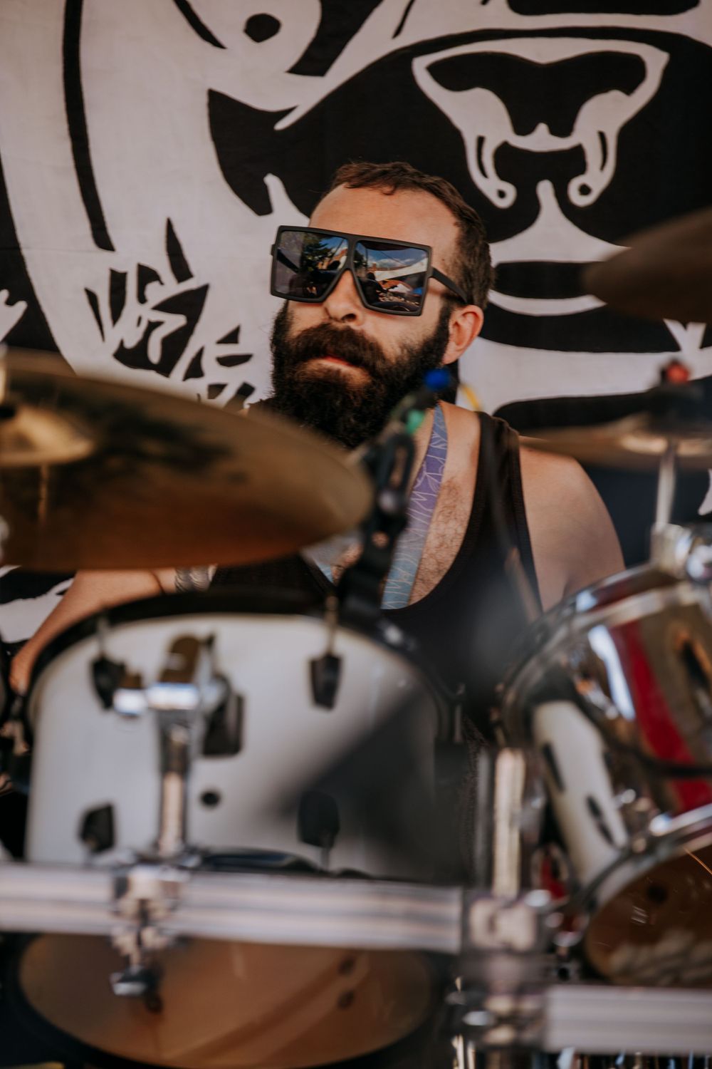 Drummer performing behind kit wearing sunglasses with tribal banner backdrop.