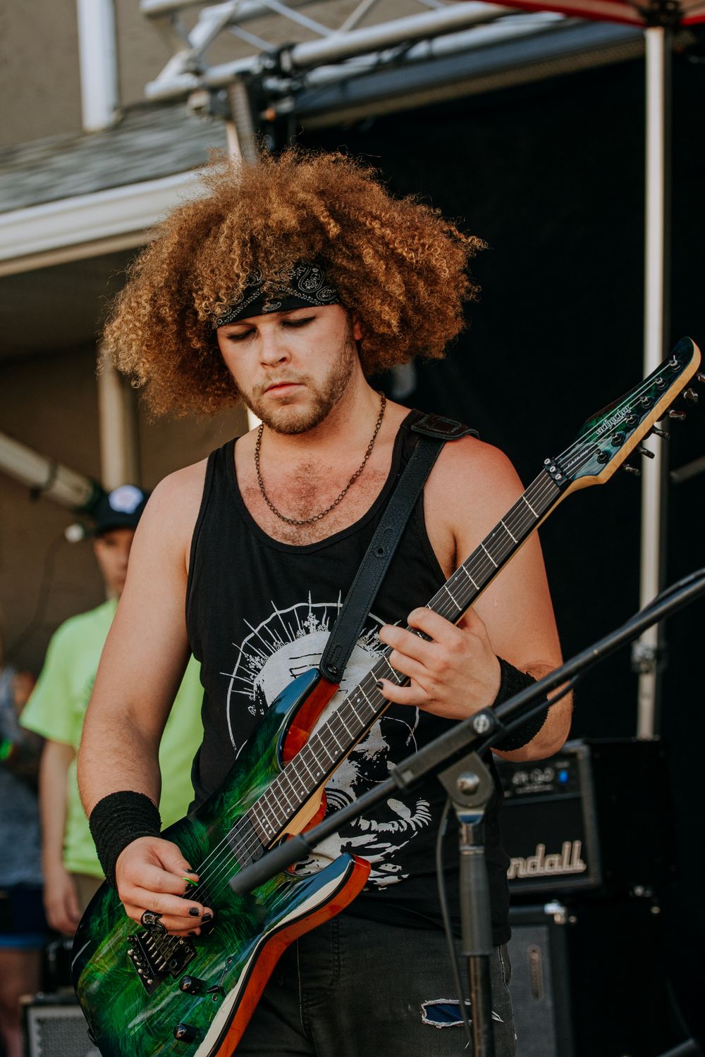 Bassist with curly hair performing in black tank top with custom painted green guitar.