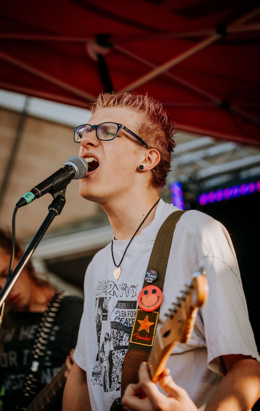 Passionate vocalist with spiked hair performing with guitar at outdoor concert venue.