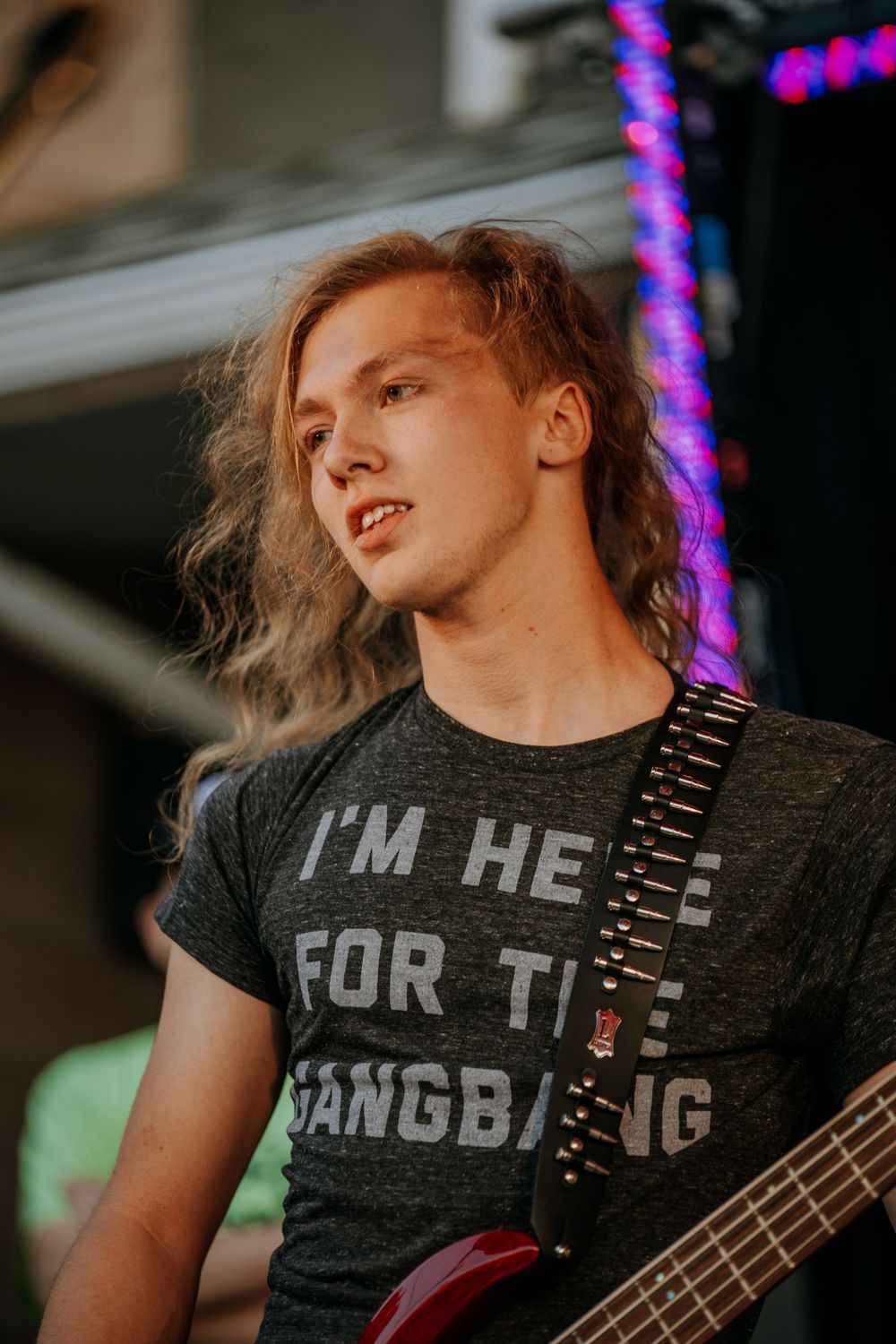 Musician with long hair performing with bass guitar under stage lighting.
