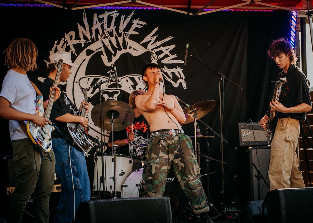 Band performing on stage with tribal graphic banner backdrop during outdoor concert.