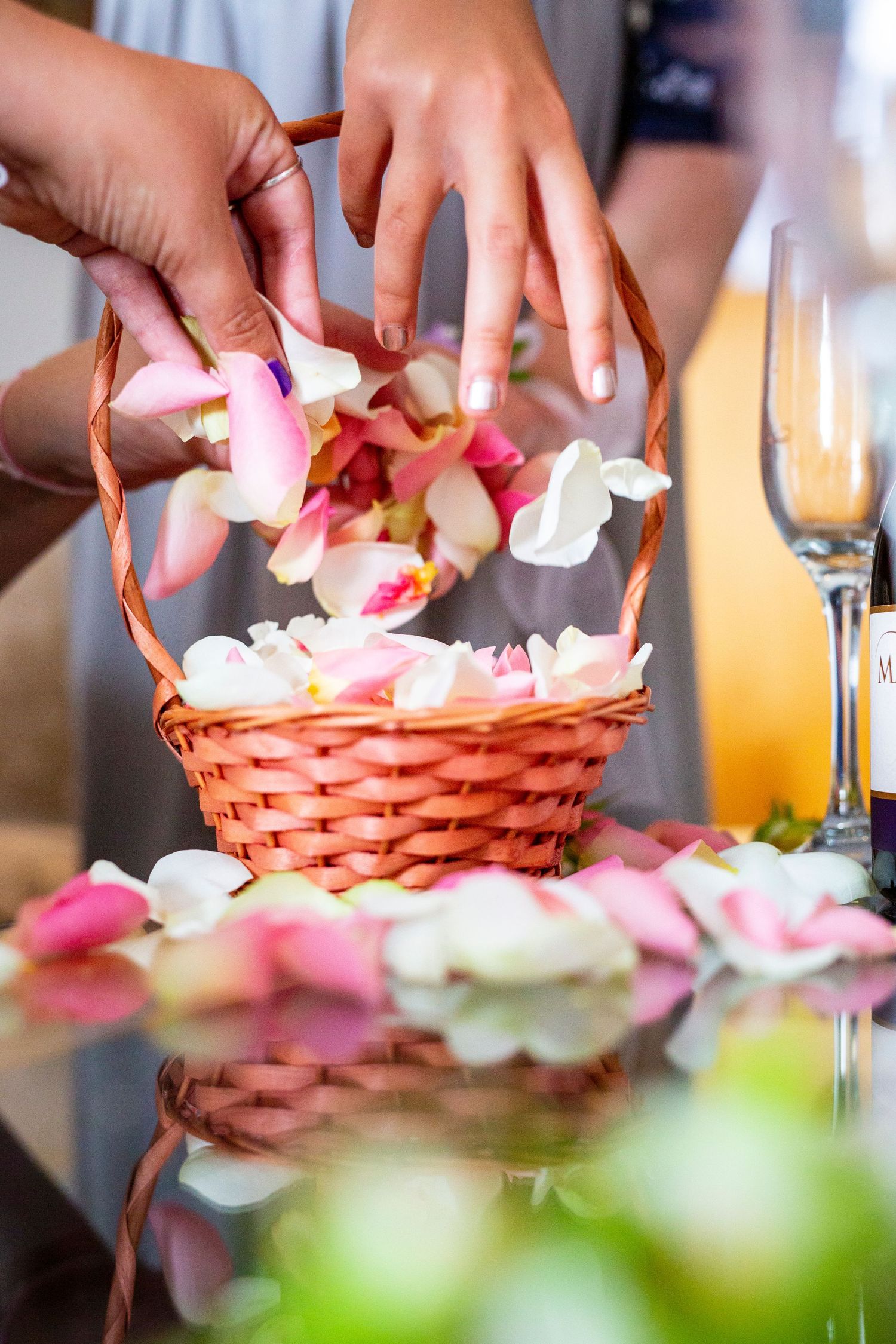 Hands placing pink and white rose petals in woven basket during wedding preparations.