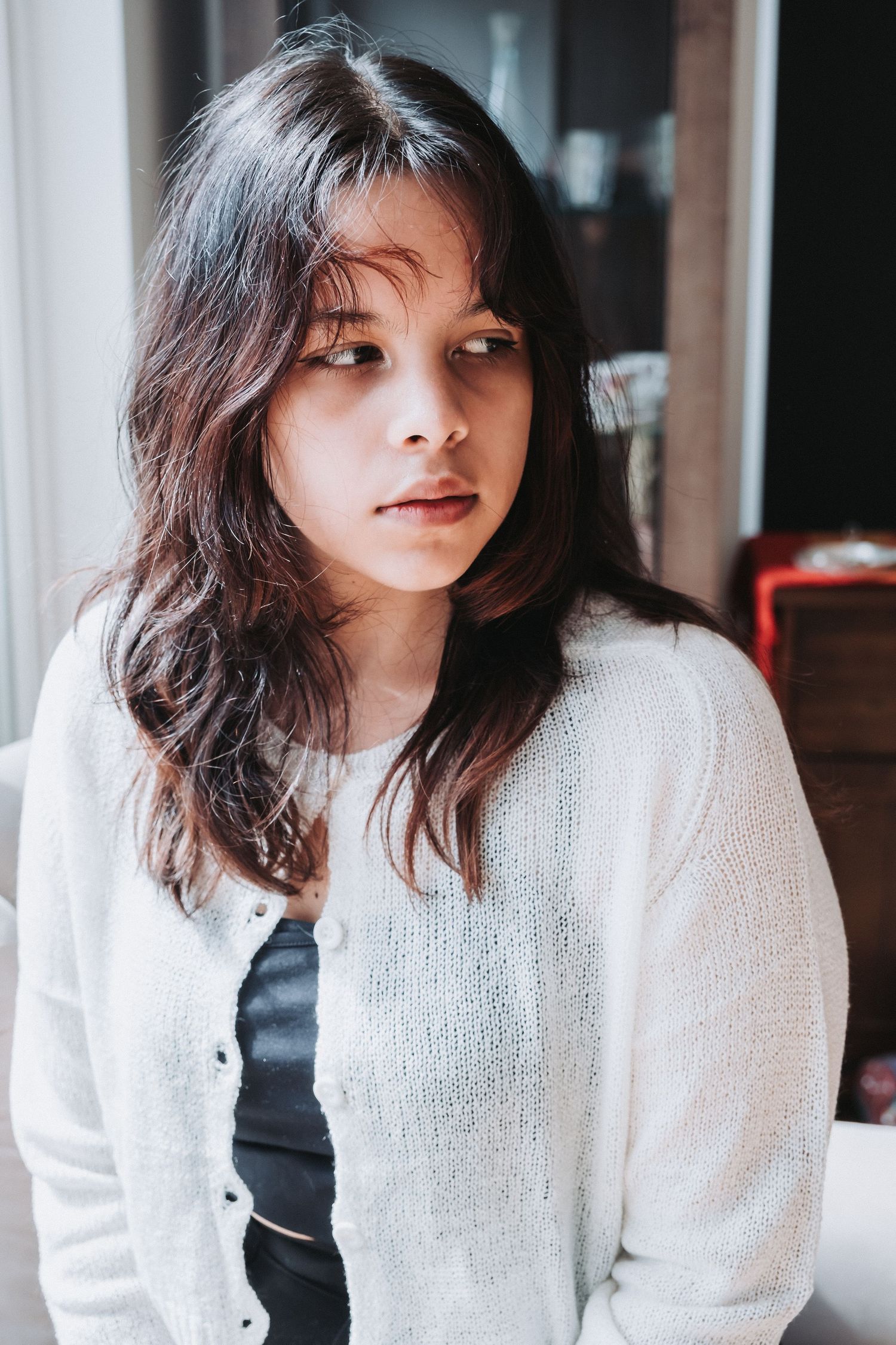 Portrait of someone in a white sweater with long dark hair gazing softly at the camera.