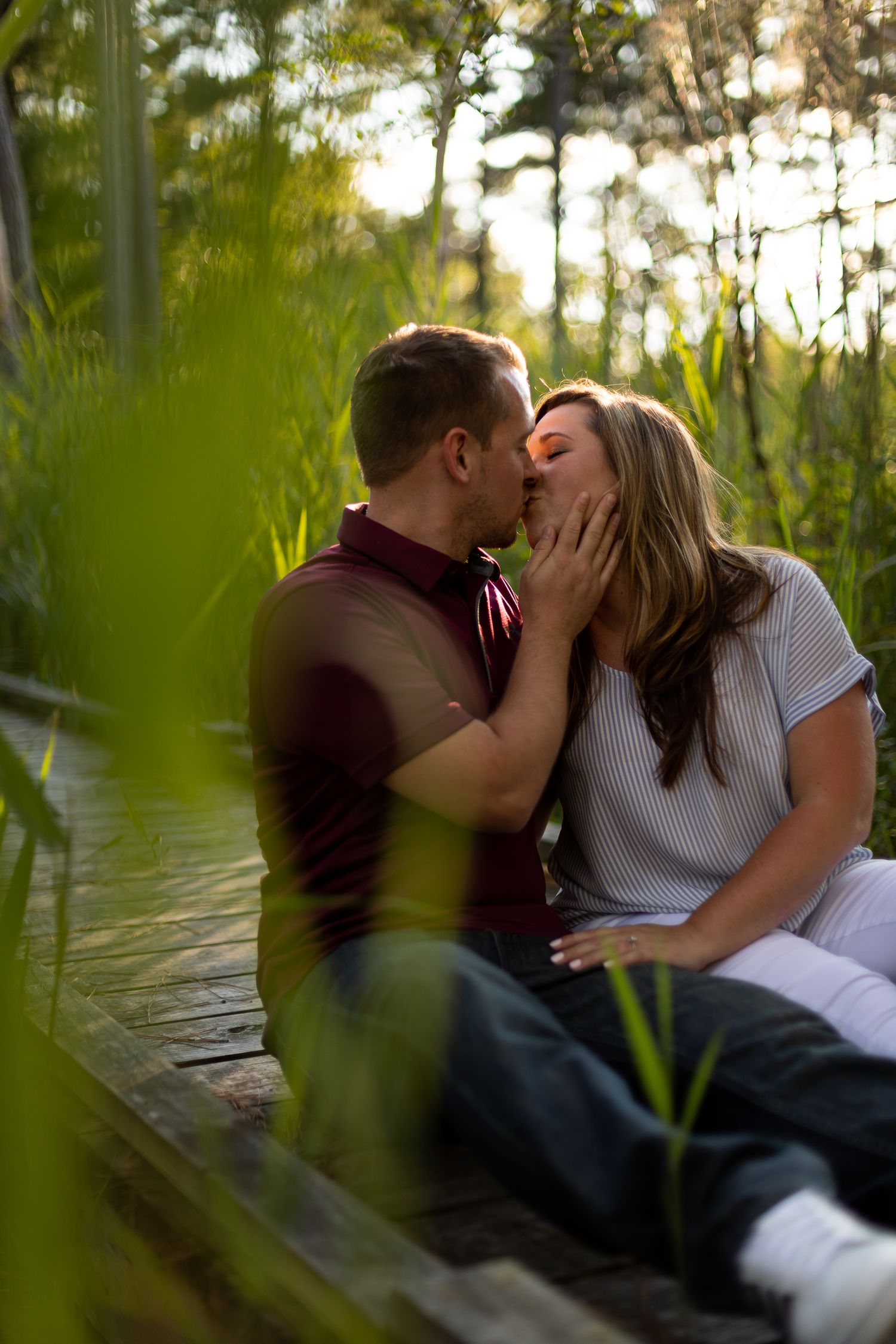 Intimate couple sharing romantic moment on wooden path surrounded by marsh grass at sunset.