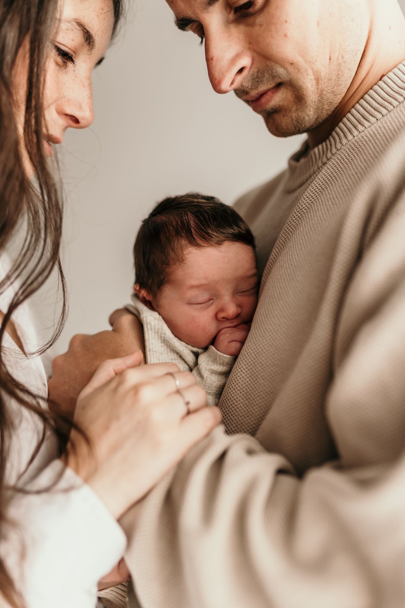 Intimate family moment with newborn baby swaddled in soft cream colored fabric.