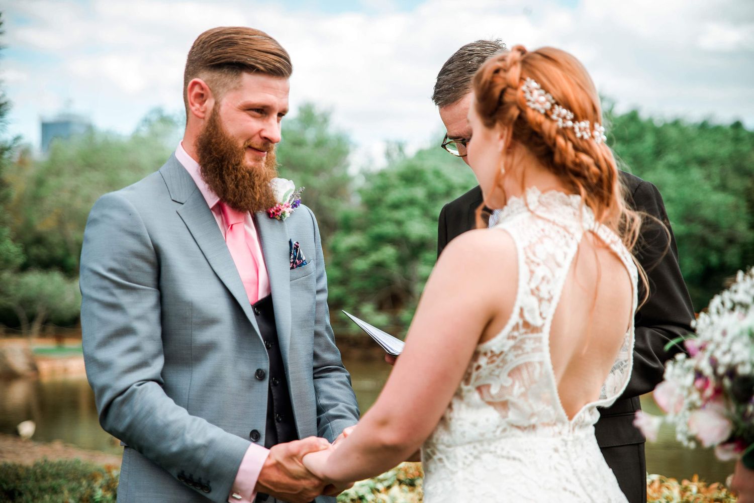 Wedding couple holding hands during outdoor ceremony with rustic garden backdrop.