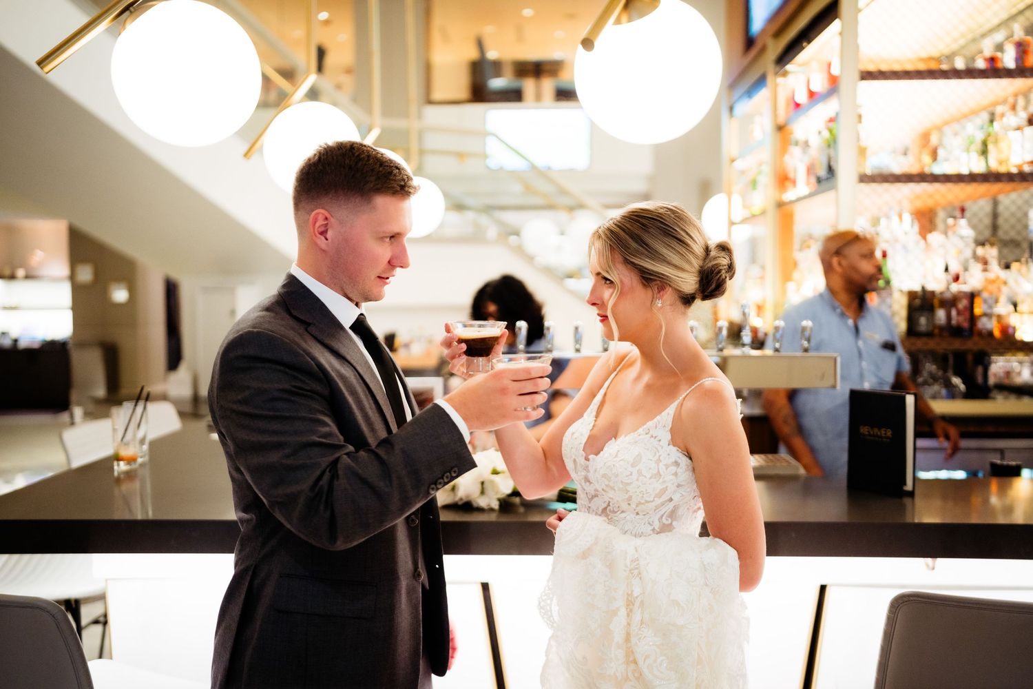 Newlyweds sharing drinks at an elegant bar setting with natural lighting.