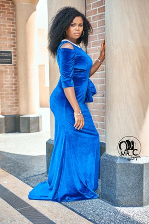 Elegant royal blue velvet evening gown with three-quarter sleeves photographed against a brick wall backdrop.