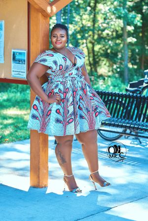 Fashionable printed dress with floral patterns and ruffled sleeves worn at an outdoor location with wooden beams and benches.