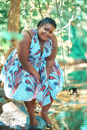 Vibrant peacock print dress photographed in dappled sunlight by water.