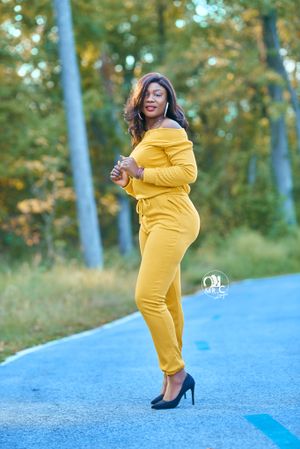 Confident pose in mustard yellow loungewear set with black heels on blue pathway.