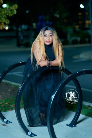 Fashion portrait in black evening gown against urban nighttime backdrop with curved metal railings.