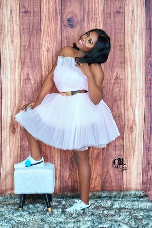 Playful pose in white tulle dress and sneakers against wooden wall background.