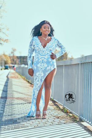 Fashion model in blue and white patterned dress posing along outdoor fence.