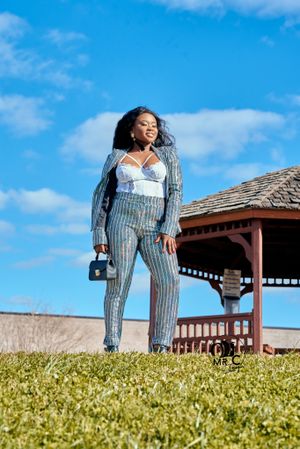 Outdoor fashion photo featuring metallic striped jumpsuit near a gazebo on grassy hill.