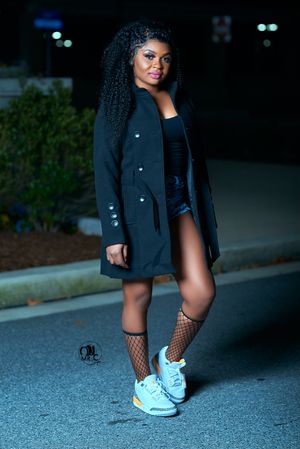 Street style shot featuring black coat, fishnet stockings and white sneakers at night.