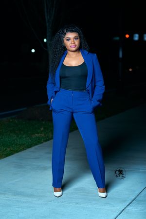 Professional fashion photo of a royal blue pantsuit with black top and white heels against a dark nighttime backdrop.