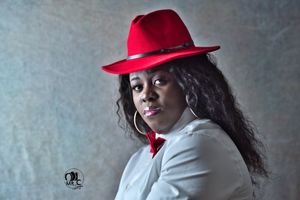 Dramatic portrait with red fedora and white shirt against grey textured background.