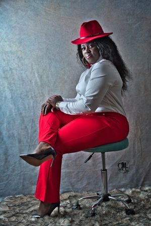 Fashion portrait featuring red pants, white shirt, and matching red fedora on a studio chair.