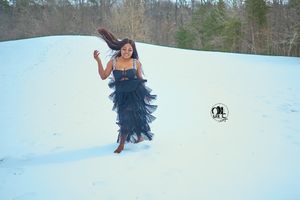 A layered navy blue evening dress flows gracefully as its wearer poses on a snow-covered hillside.