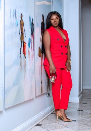 Bold red power suit with gold buttons and nude heels against abstract art wall.