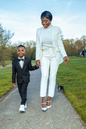 Elegant all-white ensemble with blazer and heels walking on path in spring setting.