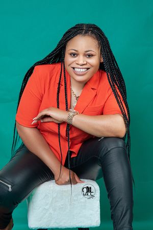 Modern fashion portrait with orange blazer, leather pants and white handbag against teal background.