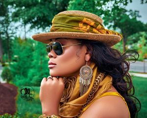 Stylish summer fashion look featuring a yellow hat, sunglasses, and statement earrings against lush greenery.