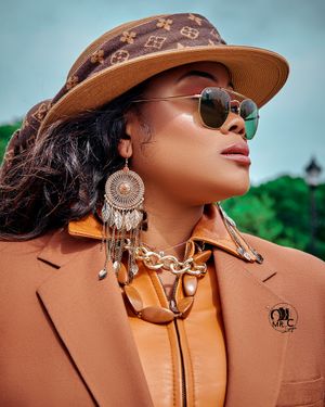 Fashion portrait featuring brown hat, statement earrings, and sunglasses with designer accessories.
