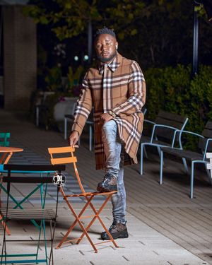 Person in plaid coat and distressed jeans poses outdoors near cafe seating.