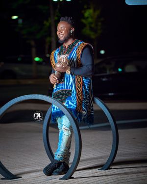 Person in blue patterned vest and ripped jeans poses near bike rack at night.