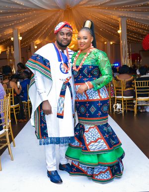 Couple wearing traditional African-inspired formal attire poses at decorated reception venue.