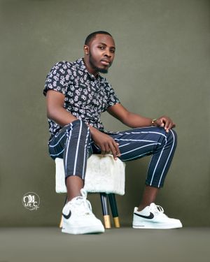 Person in floral shirt and pinstriped pants sits on white stool in studio setting.