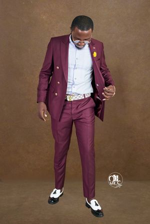 Person wearing burgundy suit and white shirt strikes dynamic pose against brown background.