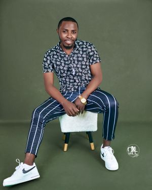 Person in patterned shirt and striped pants poses on white stool with Nike sneakers.