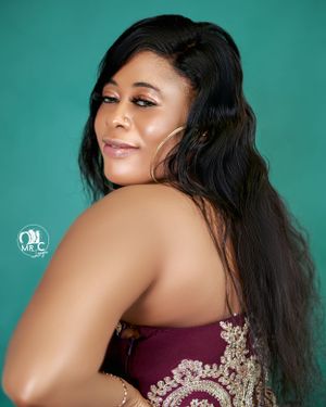 Side profile portrait against teal background featuring long dark hair and burgundy dress.