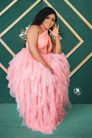 Woman in flowing pink tulle gown poses against geometric green background.