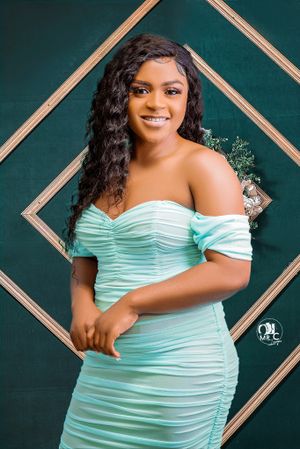 Portrait of woman in mint green off-shoulder dress against dark green geometric background.