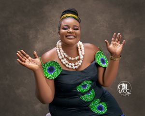 Woman in black dress with green circular patterns poses joyfully wearing pearl necklaces.