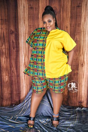 A fashion model wearing a yellow and geometric print combination outfit poses against wooden paneling.