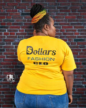 A yellow t-shirt with 'Dollars Fashion' text shown from behind against brick wall background.