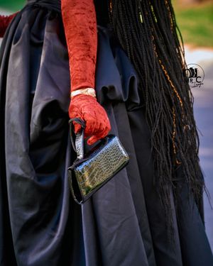 Close-up of red lace gloves holding a metallic clutch against a dark formal dress.