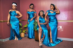 Group photo of four women wearing matching turquoise formal dresses against pink wall.