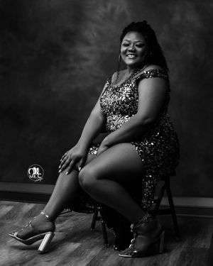 Black and white portrait of woman in sparkly dress seated on chair.