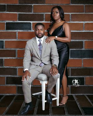 Studio portrait of couple in formal wear against brick wall backdrop.