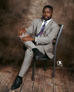 Professional portrait of man in gray suit seated on chair against textured backdrop.