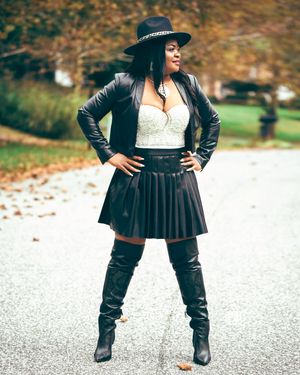 Fashion portrait of woman in leather jacket, pleated skirt and thigh-high boots on autumn road.